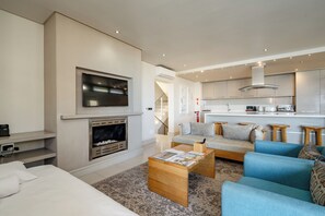 A modern living room with a fireplace, a sofa, a coffee table, and a TV mounted on the wall. - Harbour House Hotel (Hermanus)