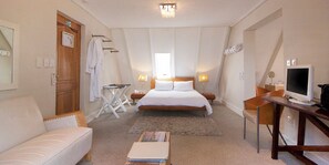 A hotel room with a bed, a desk with a computer, a chair, a small table, and a sofa. - Harbour House Hotel (Hermanus)