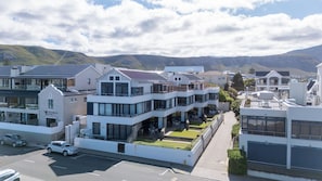 A modern residential building with multiple balconies, a driveway, and a view of the surrounding hills. - Harbour House Hotel (Hermanus)