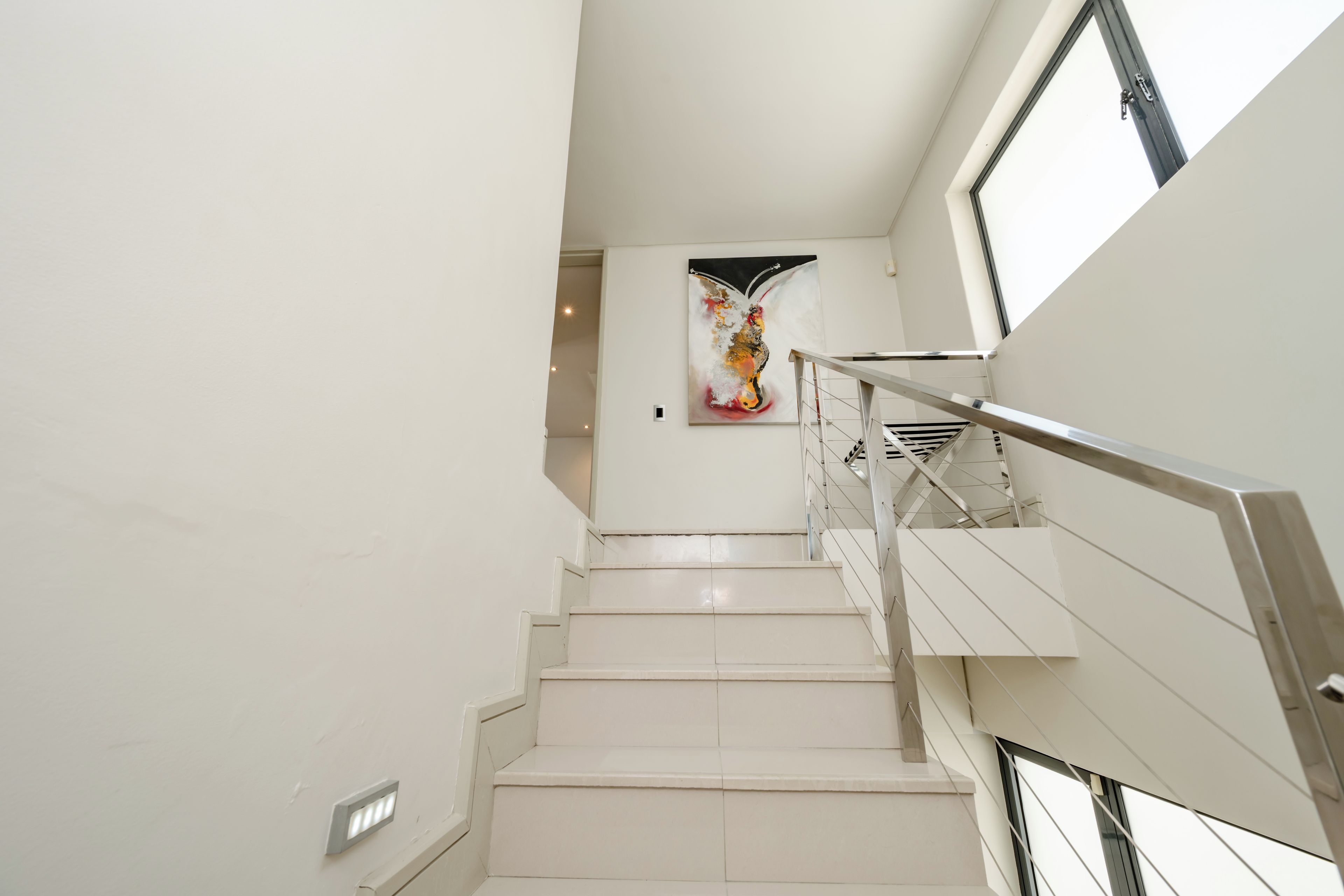 A modern staircase with a metal railing, leading to a room with a large abstract painting on the wall.