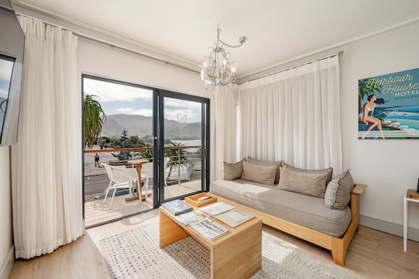 A modern living room with a sofa, coffee table, and a view of the outdoors through a sliding glass door. - Harbour House Hotel (Hermanus)
