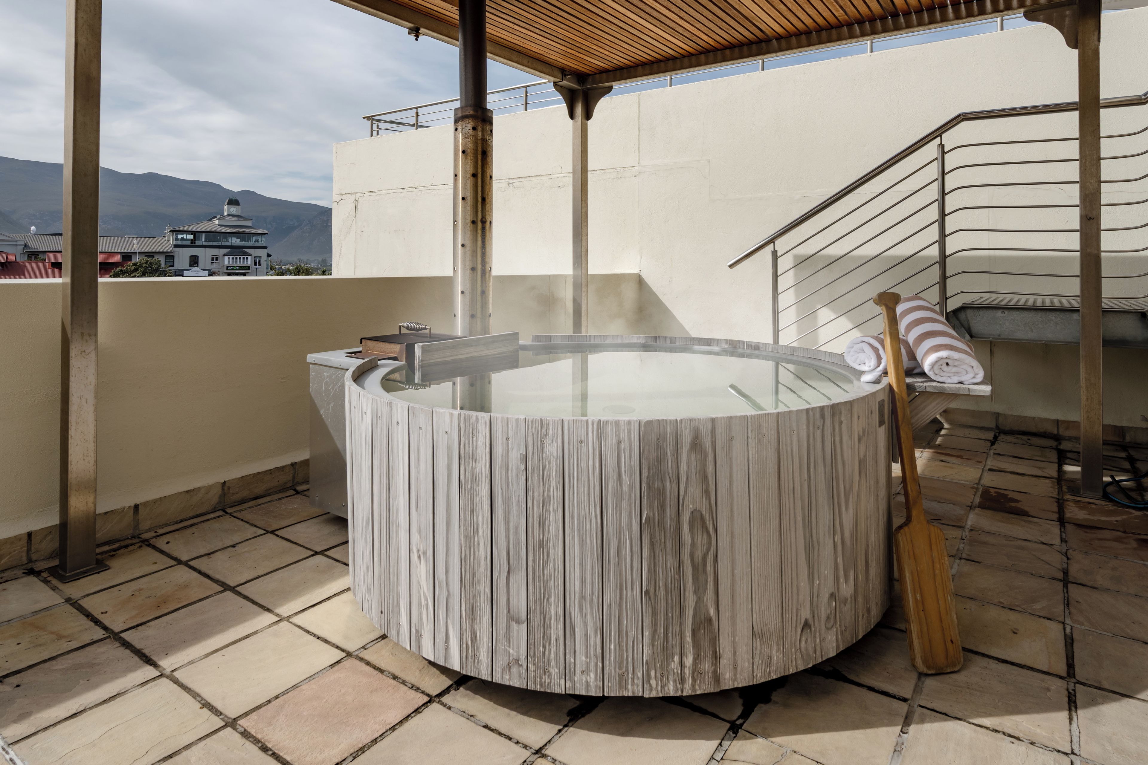 A hot tub with a wooden exterior, a wooden paddle, and a towel rack on a rooftop terrace.