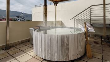 A hot tub with a wooden exterior, a wooden paddle, and a towel rack on a rooftop terrace.