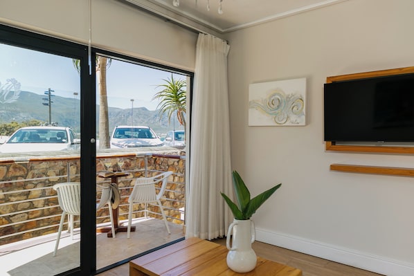 Une chambre avec un balcon, une télévision, un tableau et une plante en pot.