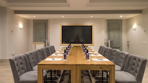 A conference room with a long table, grey upholstered chairs, a large screen, and wall-mounted lighting. - Harbour House Hotel (Hermanus)