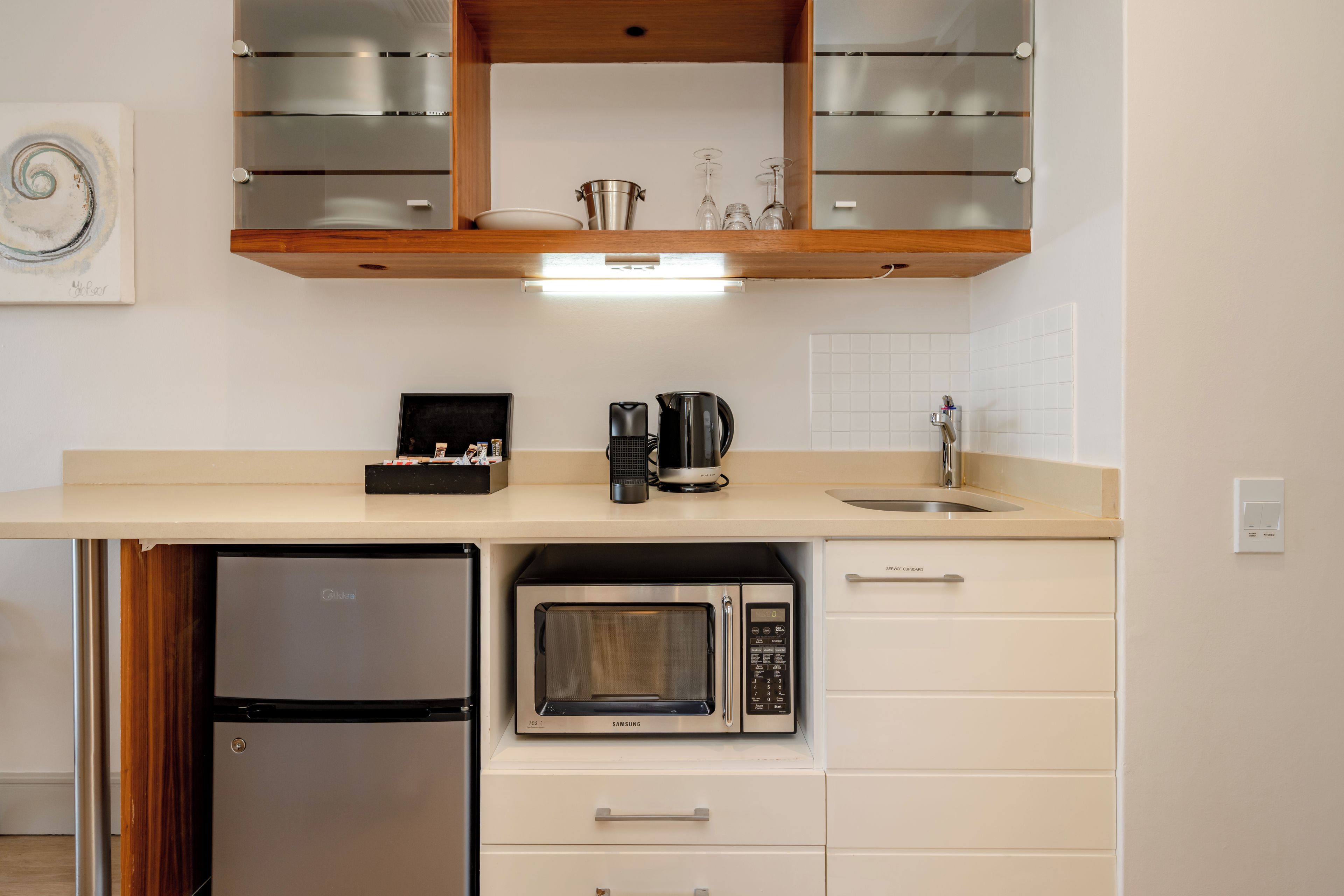 Una cocina compacta con microondas integrado, cafetera y un refrigerador pequeño.