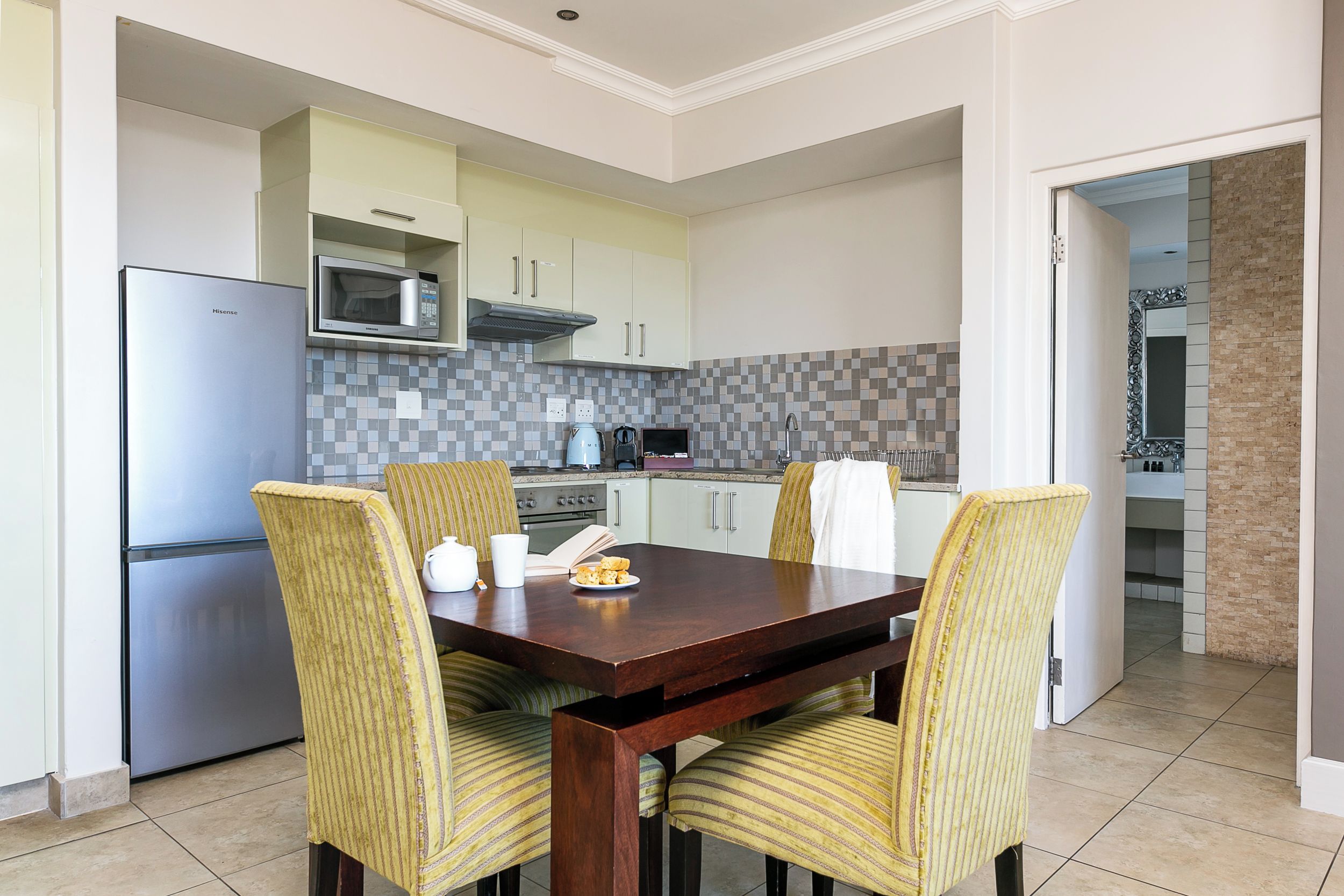 Een moderne keuken met een ingebouwde magnetron, een roestvrijstalen koelkast en een eethoek met een houten tafel en streepstoelen.