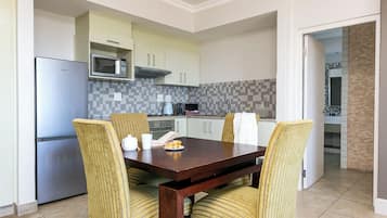 Een moderne keuken met een ingebouwde magnetron, een roestvrijstalen koelkast en een eethoek met een houten tafel en streepstoelen.
