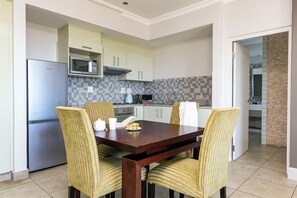 A modern kitchen with a built-in microwave, a stainless steel refrigerator, and a dining area with a wooden table and striped chairs. - Harbour House Hotel (Hermanus)