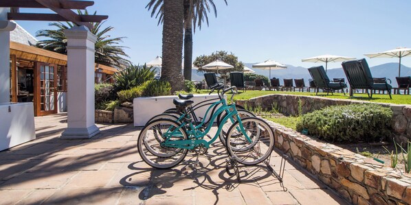 Un vélo est garé sur une terrasse en pierre, d’où l’on aperçoit une piscine et des chaises longues.