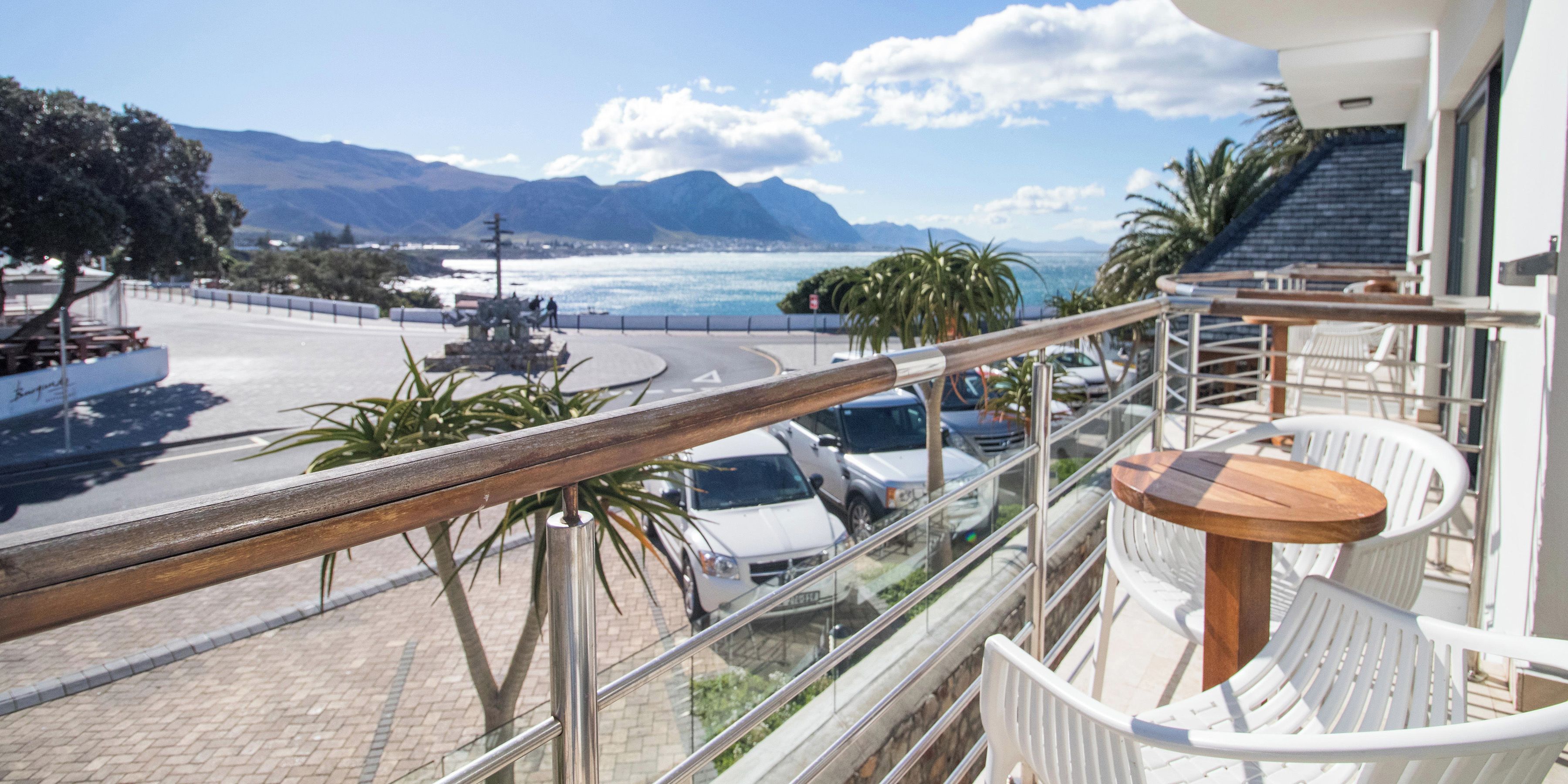 A balcony with a view of the sea, a round wooden table, and a white chair.