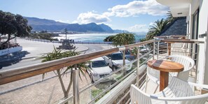 A balcony with a view of the sea, a round wooden table, and a white chair. - Harbour House Hotel (Hermanus)