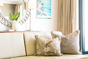 A beige sofa with floral cushions, a mirror with a chain design, a potted plant, and a poster on the wall. - Harbour House Hotel (Hermanus)