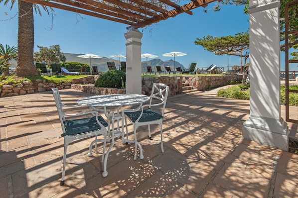 An outdoor patio with a table and chairs, surrounded by stone walls and palm trees. - Harbour House Hotel (Hermanus)