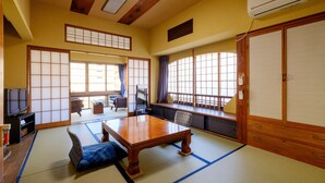 A traditional Japanese room with tatami flooring, a wooden table, a television, and sliding doors. - Kiya Ryokan (Misasa)