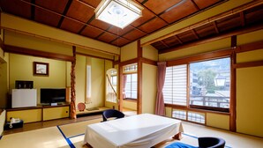 A traditional Japanese room with tatami flooring, a bed, a television, and a view of the outside. - Kiya Ryokan (Misasa)