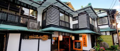 A traditional Japanese building with a wooden balcony, a green roof, and a sign with Japanese characters.