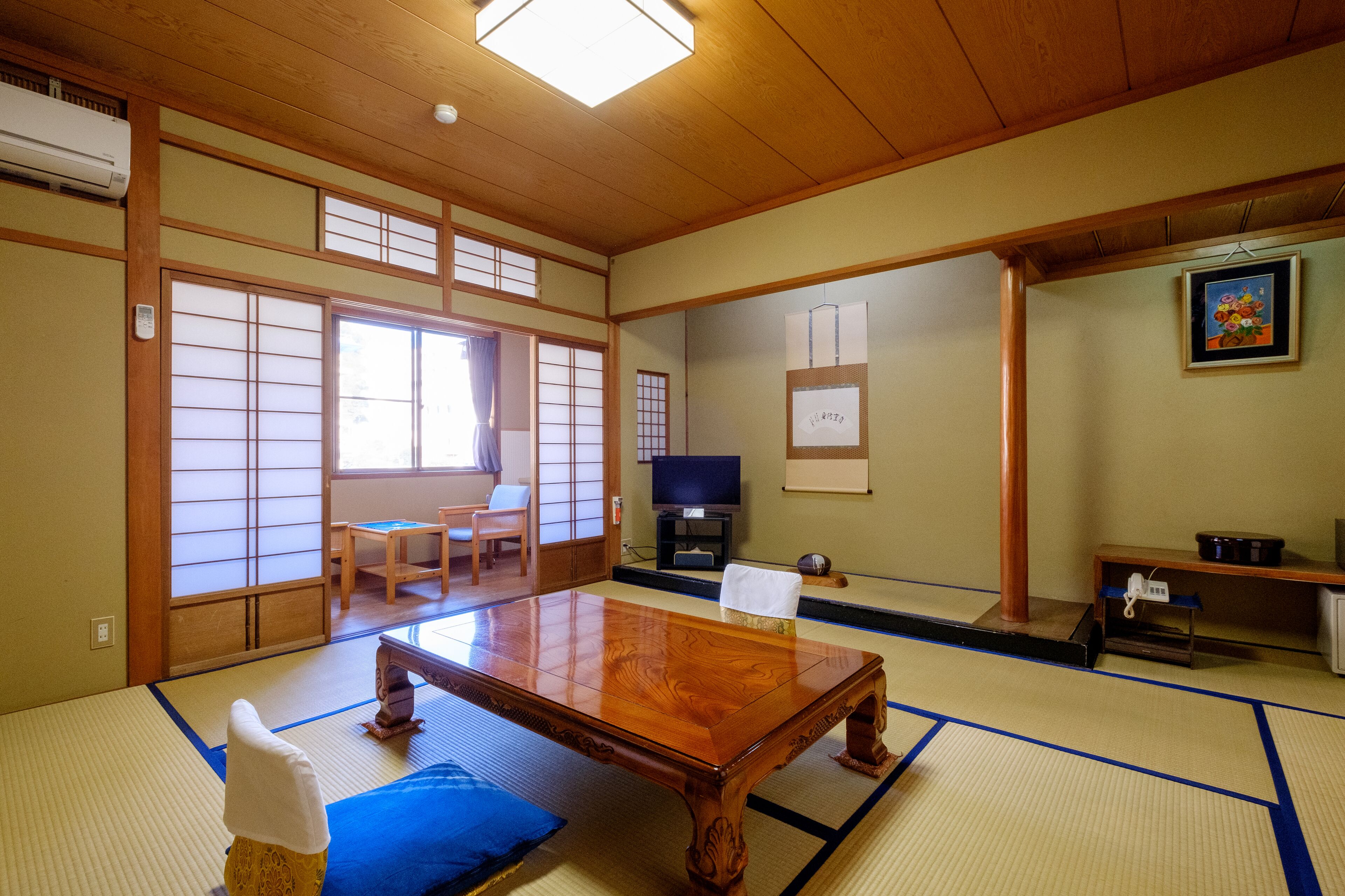 Una habitación japonesa tradicional con suelo de tatami, una mesa de madera baja, un televisor y puertas correderas.