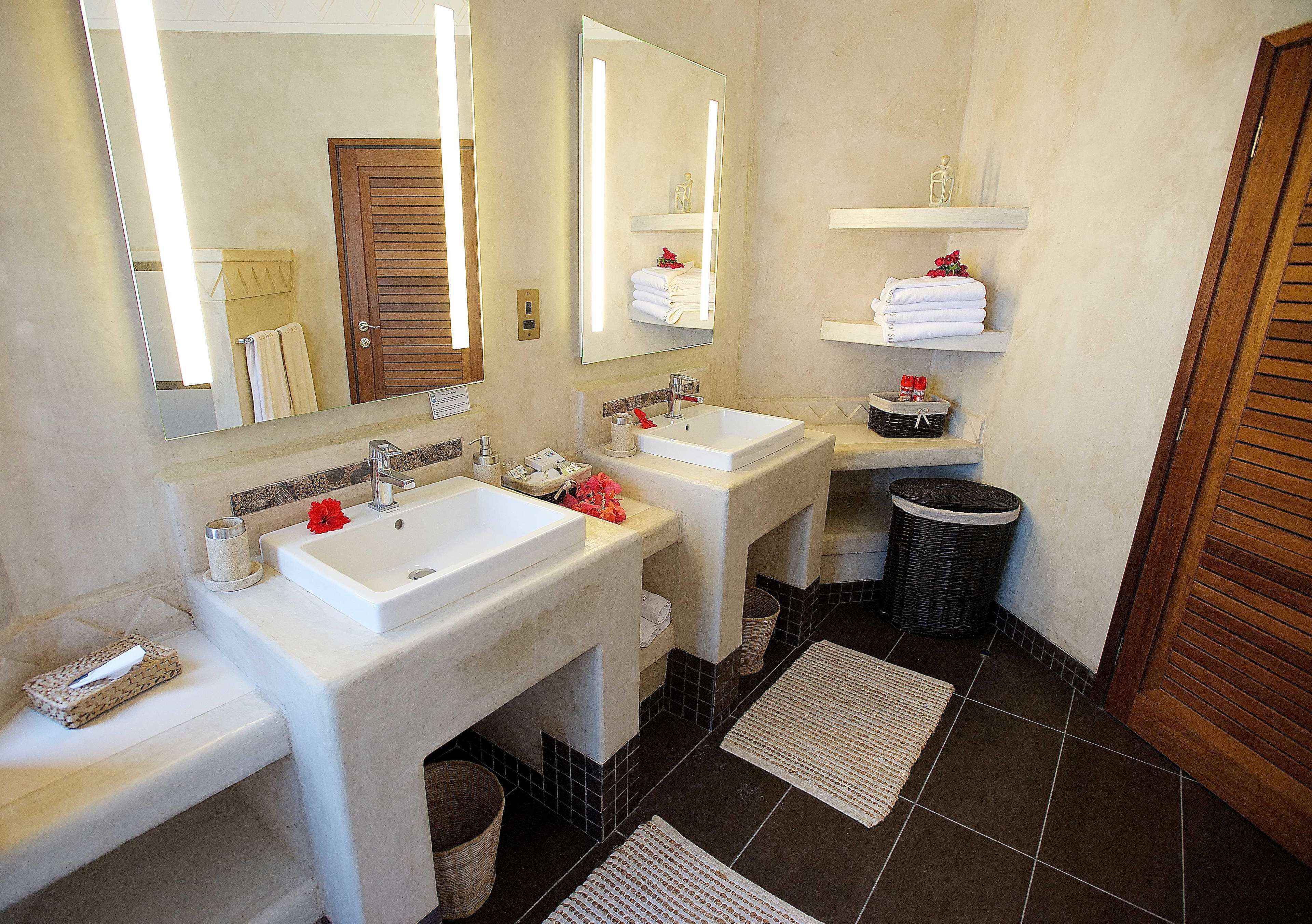 Une salle de bain avec deux lavabos, un miroir et un espace douche. Des serviettes et des articles de toilette sont disposés sur des étagères.