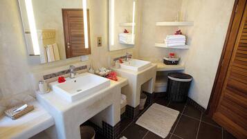 Une salle de bain avec deux lavabos, un miroir et un espace douche. Des serviettes et des articles de toilette sont disposés sur des étagères.