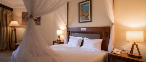 A hotel room with a bed, a nightstand with a lamp, a telephone, and a painting on the wall.