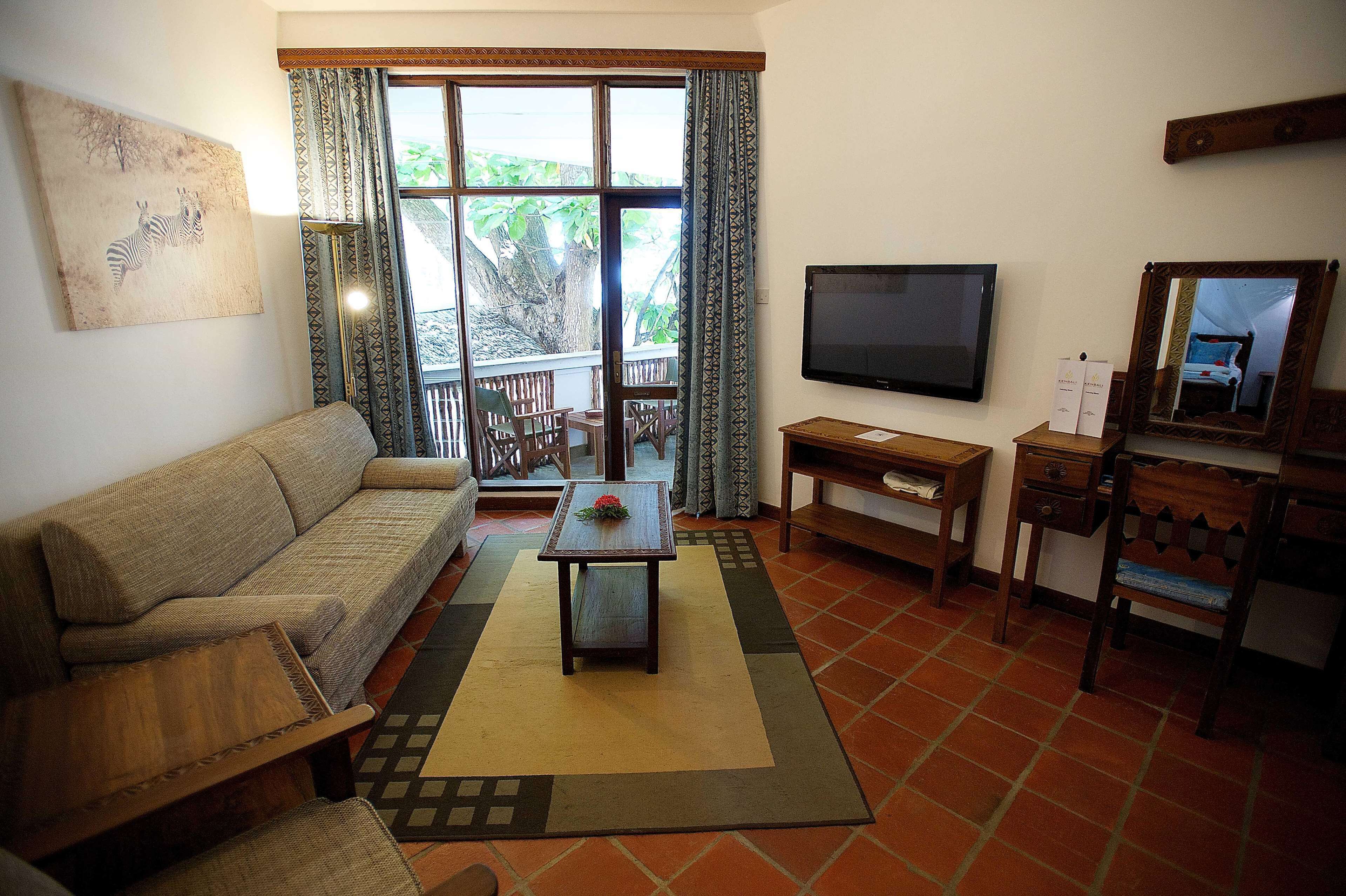 A living room with a sofa, a coffee table, a TV, and a balcony with a view of trees.