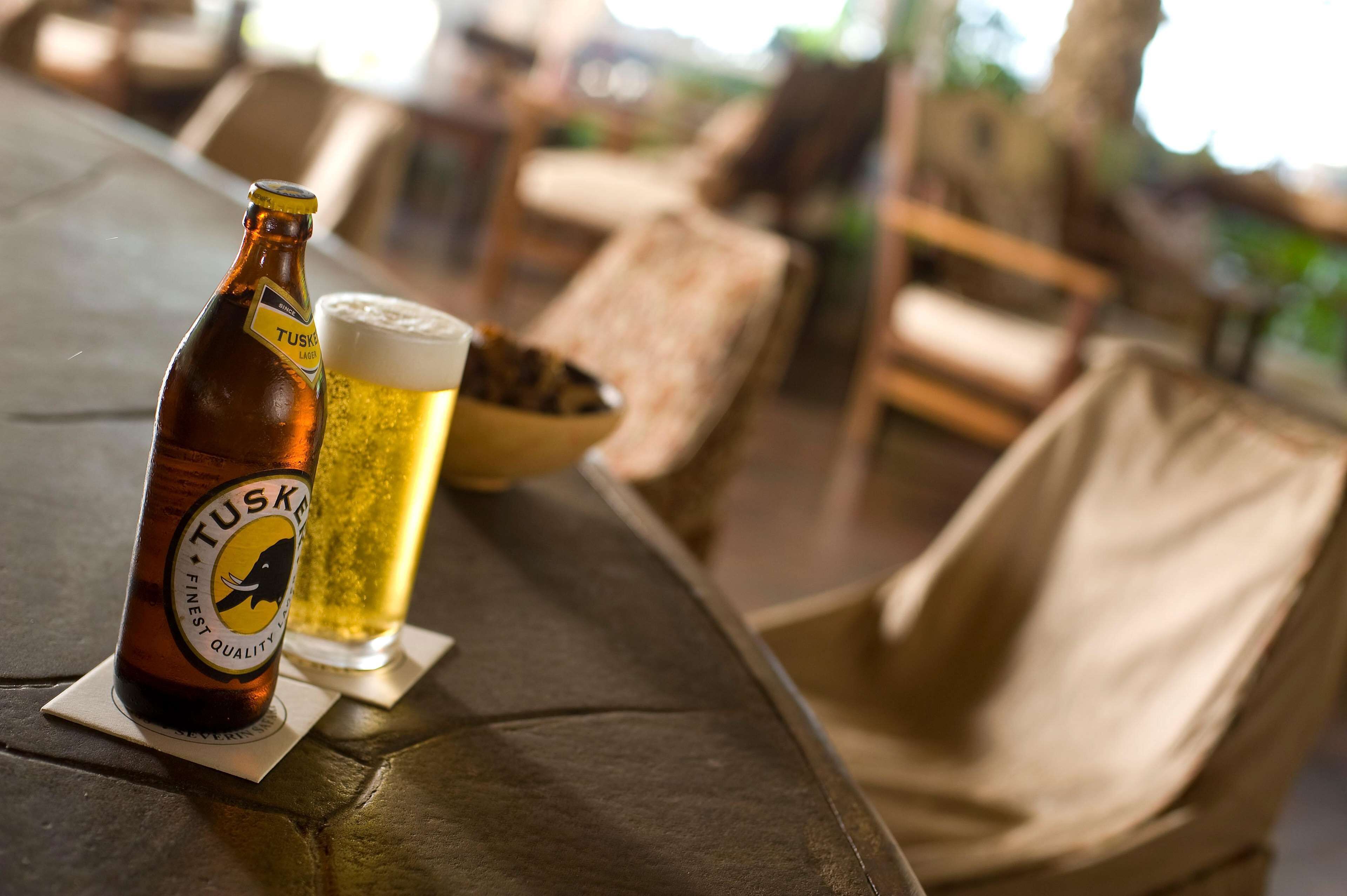 A bottle of Tusker beer and a glass of beer on a table in a restaurant setting.