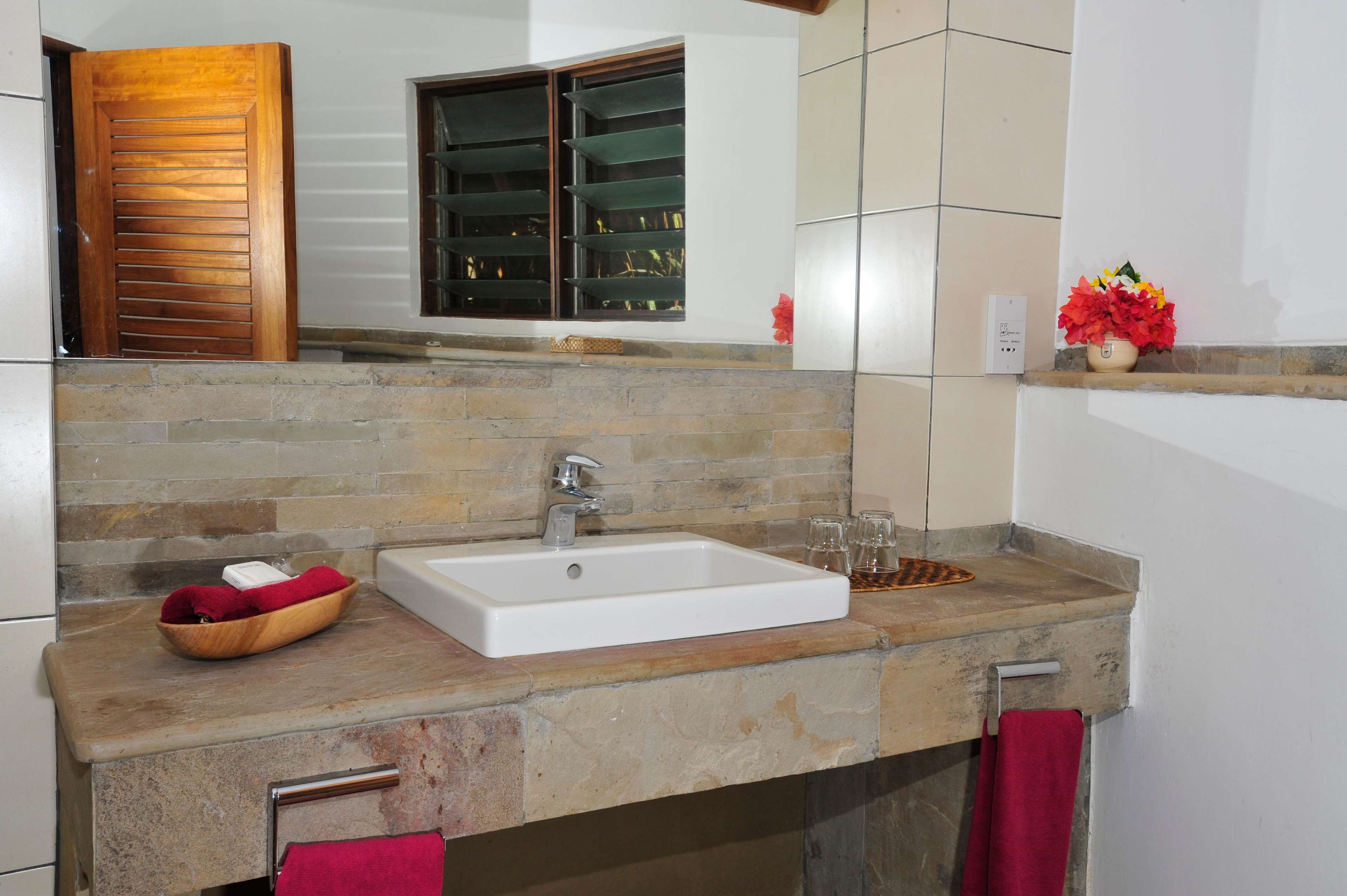 A bathroom with a stone countertop, a white sink, a wooden door, and a window with shelves.