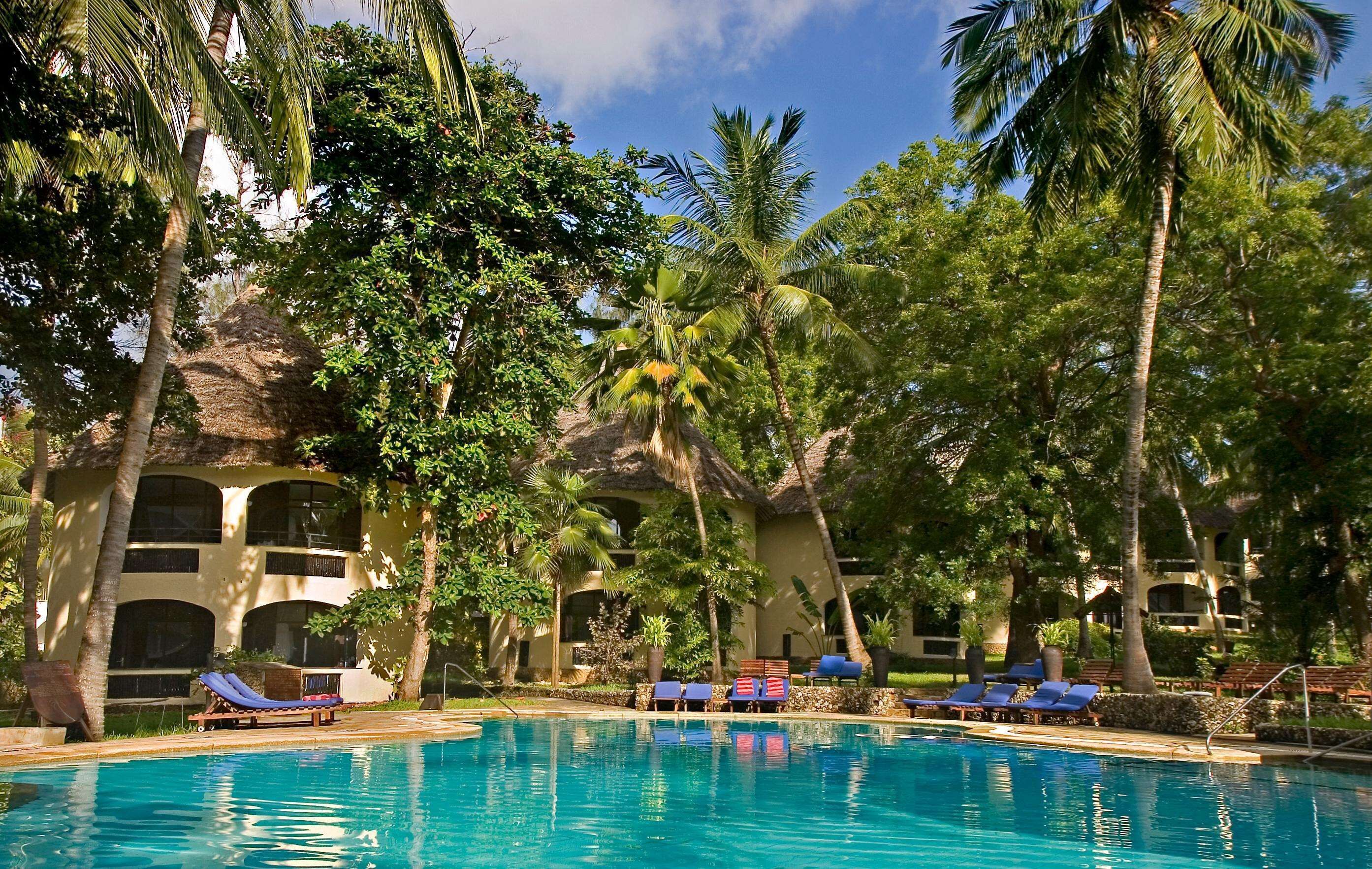 Un área de piscina con sillas de descanso y palmeras.