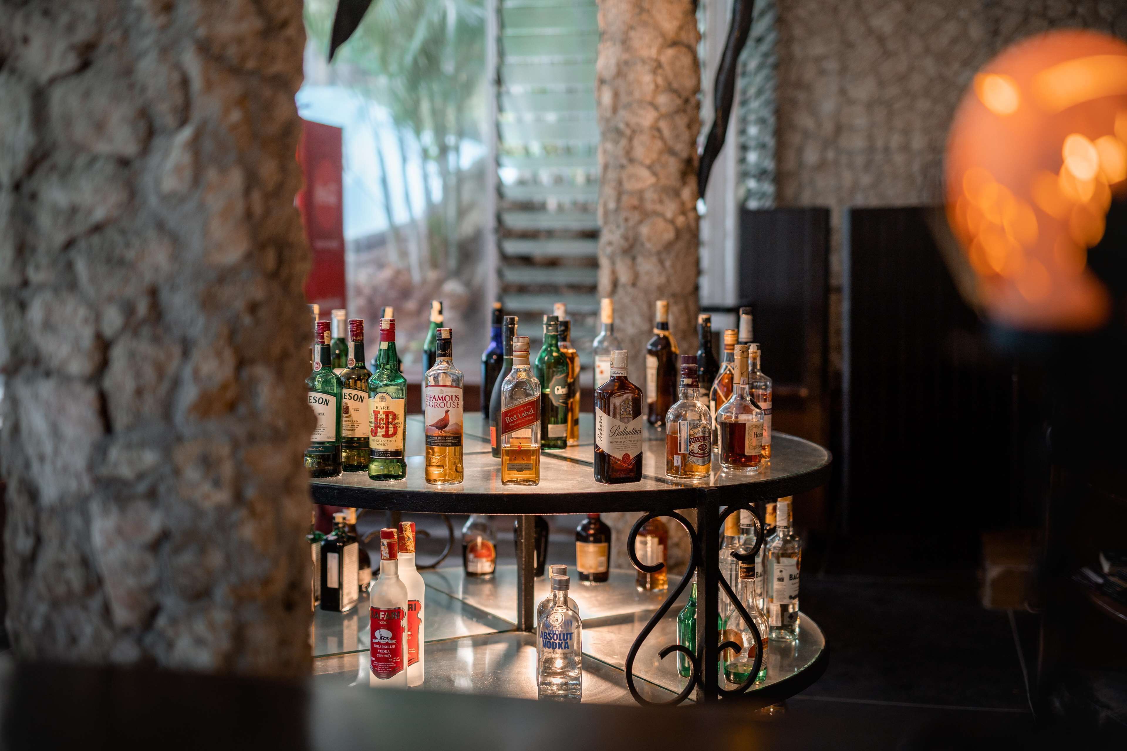 Zona de bar con una variedad de botellas de licores sobre una mesa redonda, rodeada de pilares de piedra.