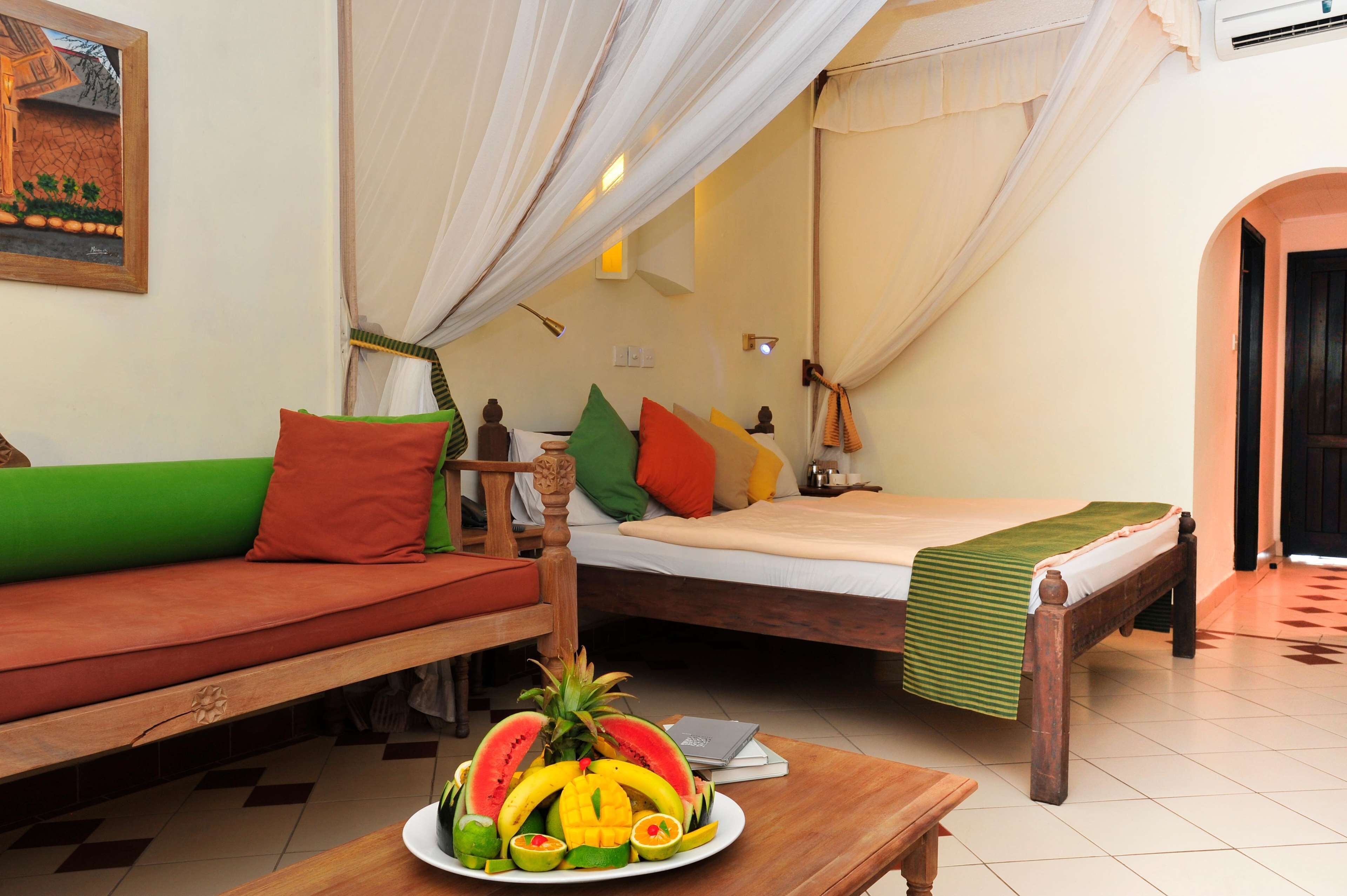 A room with a bed, a sofa, and a table with fruit.