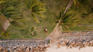 An aerial view of a beach with palm trees, a stone wall, and ocean waves. - Severin Sea Lodge (Mombasa)