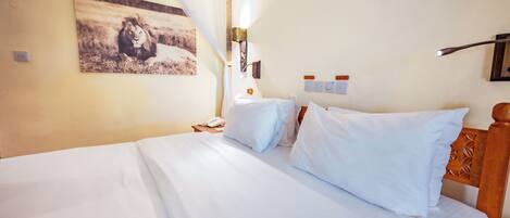 A hotel room with a large bed, a bedside table with a lamp, a wall-mounted phone, and a picture of a lion.