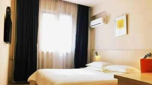 Une chambre d’hôtel équipée d’un lit, d’un bureau, d’un appareil de climatisation et d’une fenêtre avec des rideaux.