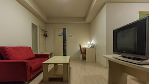 A living room with a red sofa, a TV on a stand, a small table, and a door leading to another room. - Jinjiang Inn (Beijing Tian'anmen Square Hepingmen Subway Station) (Beijing)