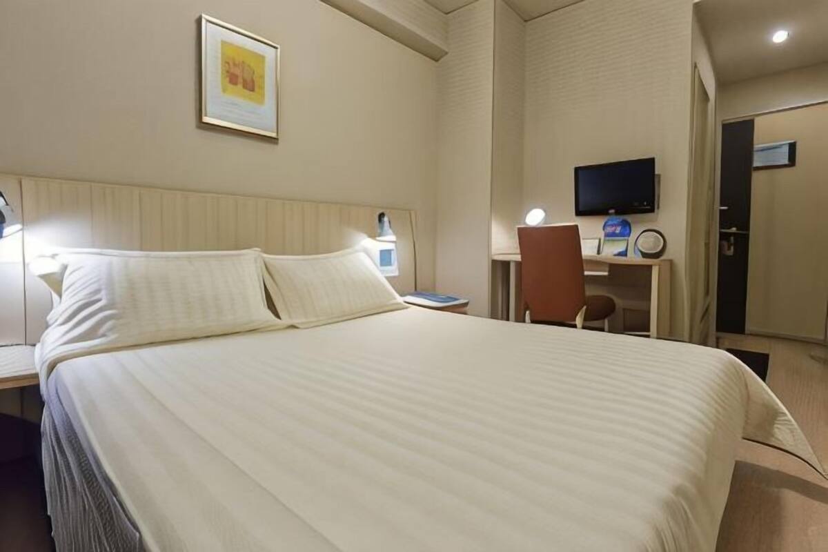 Ein Hotelzimmer mit einem großen Bett, einem Schreibtisch mit Stuhl, einem Fernseher und einer Tür.