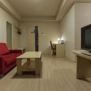A room with a red sofa, a wooden table, a TV on a stand, and a door with a sign. - Jinjiang Inn (Beijing Tian'anmen Square Hepingmen Subway Station) (Beijing)