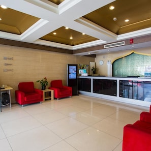 A hotel lobby with a reception desk, two red armchairs, a small table with a plant, and a clock on the wall. - Jinjiang Inn (Beijing Tian'anmen Square Hepingmen Subway Station) (Beijing)