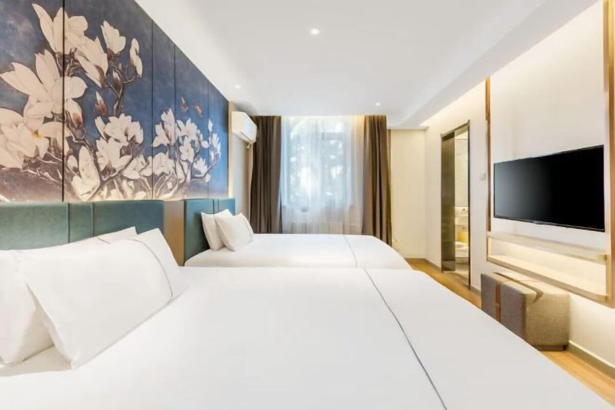 A hotel room with two beds, a large wall-mounted TV, and a painting.