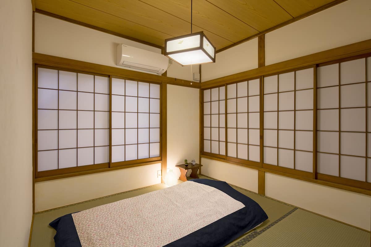 A traditional Japanese room with tatami flooring, shoji screens, and a futon bed.