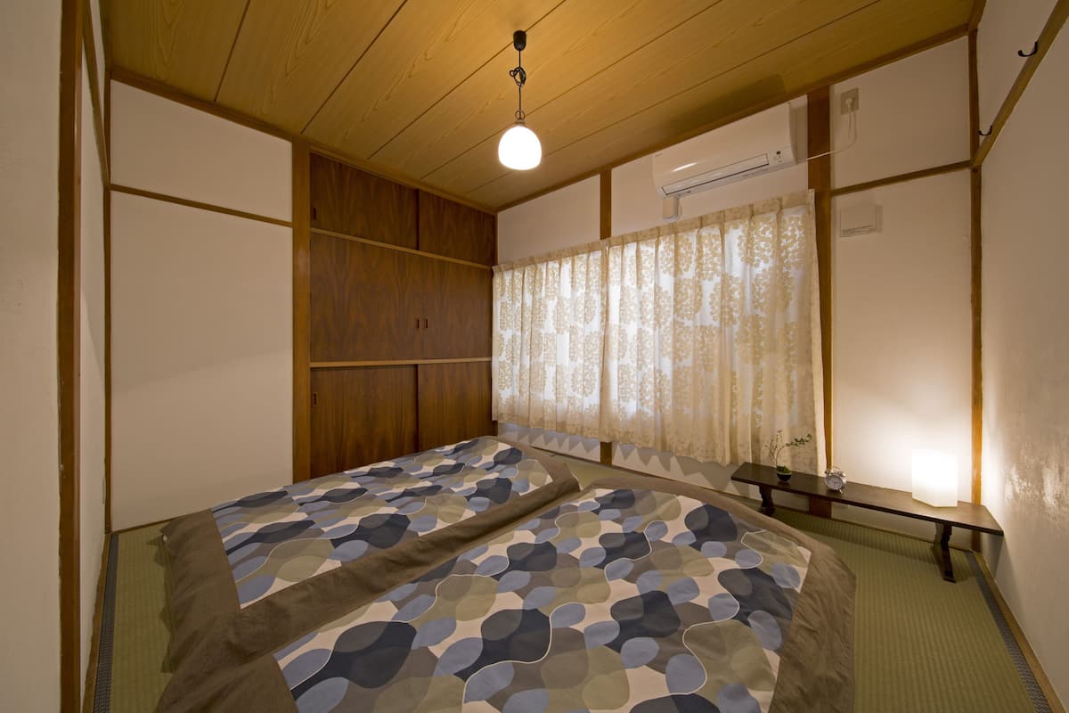 A bedroom with a bed, wooden paneling, a bedside table with a lamp, and a window with curtains.