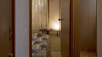 A narrow hallway leading to a bedroom with a bed, a bedside table, and a lamp.
