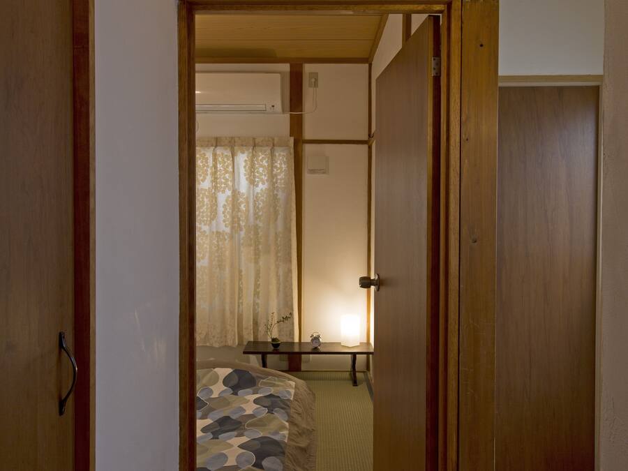 A narrow hallway leading to a bedroom with a bed, a bedside table, and a lamp.