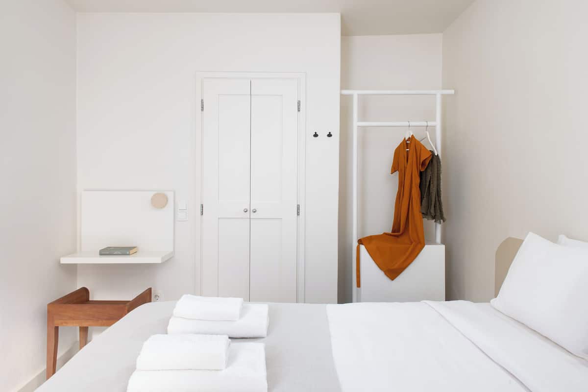 Un dormitorio con una cama, un armario, una estantería con un libro y una percha con ropa.