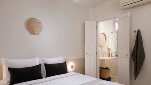 Una habitación de hotel con una cama, una lámpara de noche, un estante en la pared y un baño visible a través de una puerta abierta.