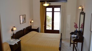 A hotel room with a bed, bedside table, lamp, and a window with curtains. - Electra (Syros)