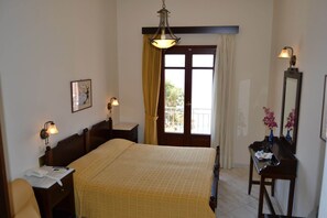 A hotel room with a bed, bedside table, lamp, and a window with curtains. - Electra (Syros)