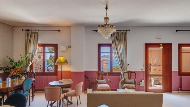 A hotel room with a dining area, a sofa, a chandelier, and a view of the outside. - Electra (Syros)