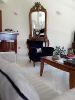 Una sala de estar con un espejo grande, un sillón azul oscuro, una mesa de centro de madera y un sofá blanco.