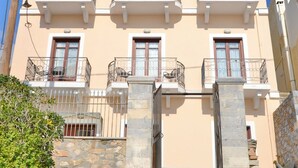 A multi-story building with balconies, stone steps leading to the entrance, and a clear sky. - Electra (Syros)